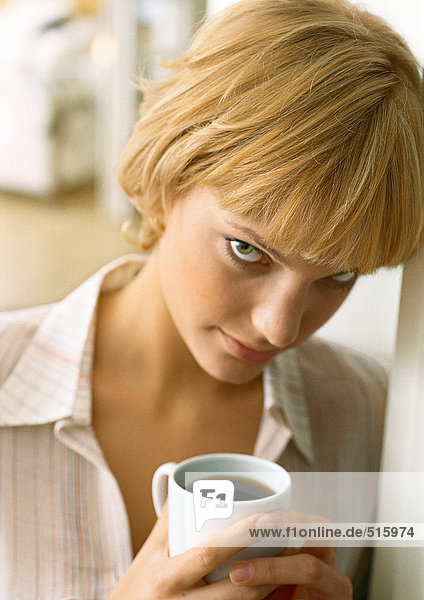 Teen girl resting head against wall  holding coffee  looking up at camera