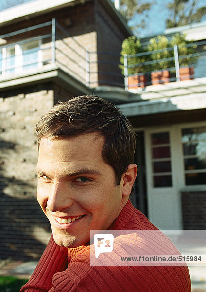 Young man in front of house  smiling over shoulder at camera