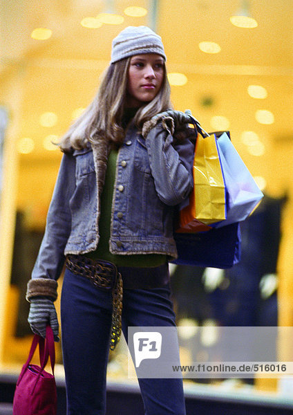Girl holding shopping bags  standing in front of store window.