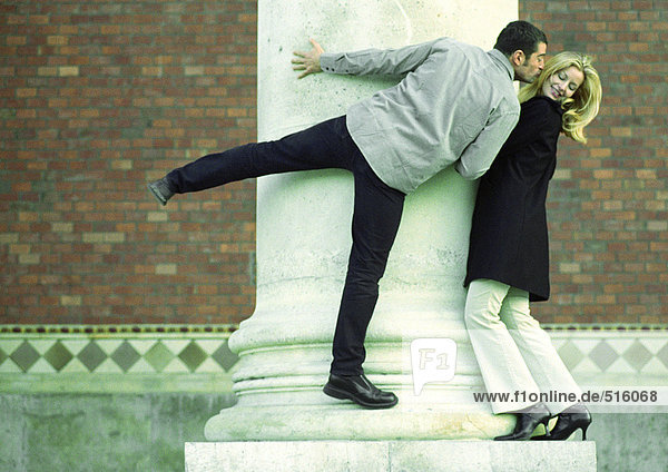 Couple standing on column  man stretching to kiss woman's cheek