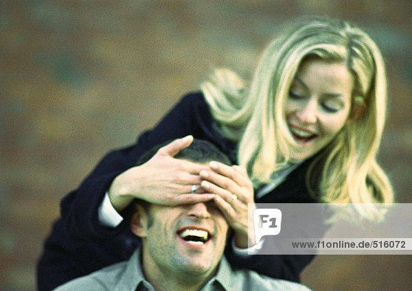 Woman covering man's eyes from behind with her hands