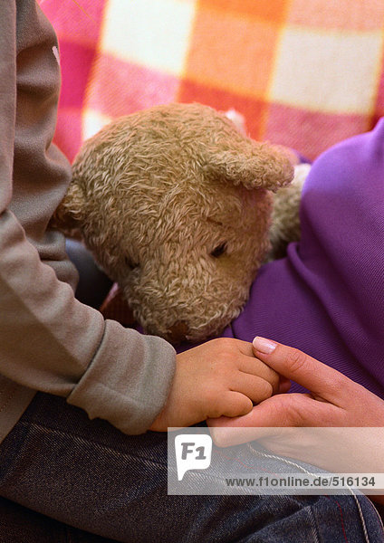 Frau und Kind halten Händchen  Teddybär zwischen ihnen