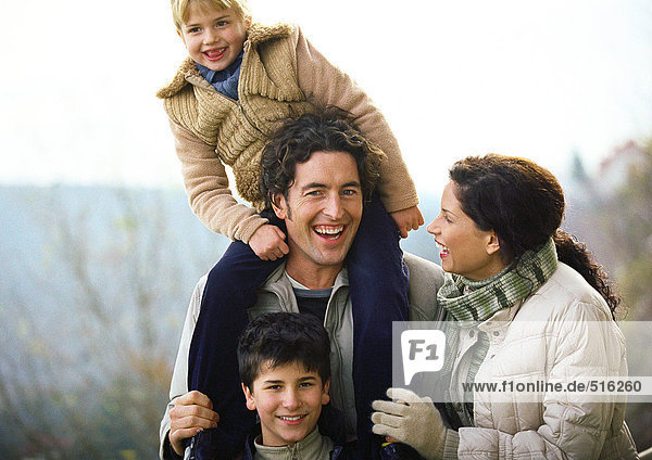 Adult woman and adult man standing outside with two children  little girl on man's shoulders  portrait