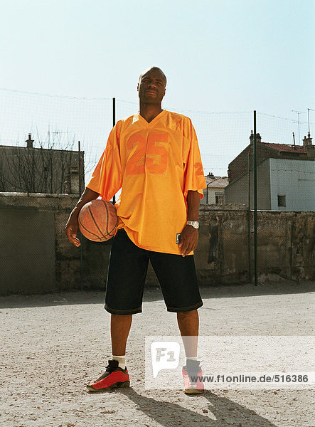 Mann stehend mit einem Basketball auf einem städtischen Spielplatz