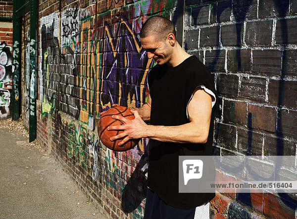 Man leaning on graffitied wall  looking down  holding basketball
