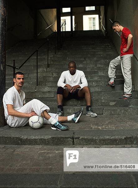Drei Männer sitzen auf einer Treppe mit Fußball