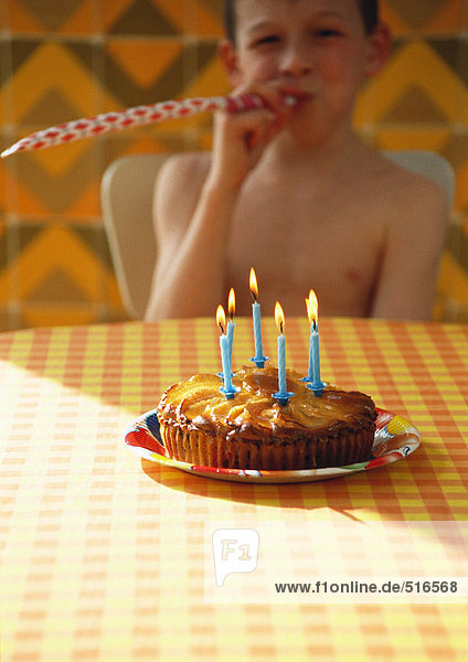 Kleiner Junge mit Geburtstagskuchen und Partyhornbläser