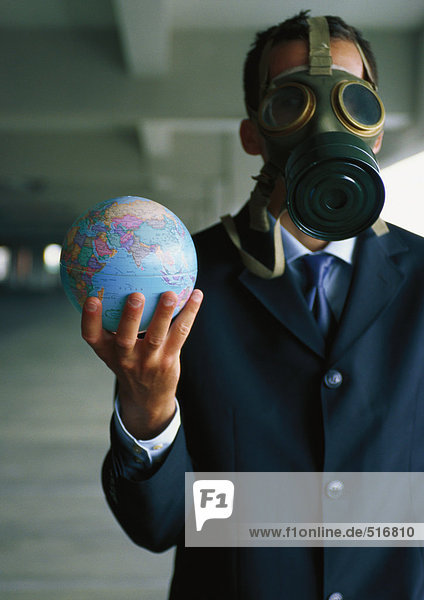Geschäftsmann hält den Globus in der Hand und trägt eine Gasmaske über dem Gesicht.