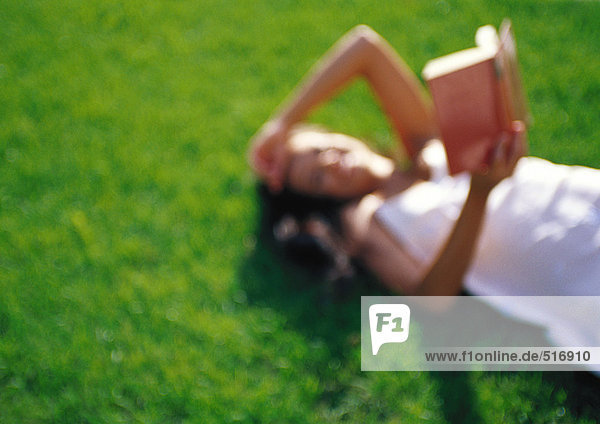 Frau auf Gras liegend,  lesend,  defokussiert