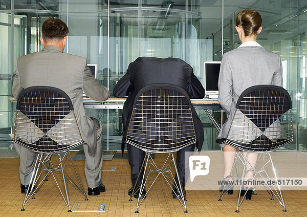 Drei Geschäftsleute sitzen Seite an Seite mit Computern  einer mit Kopf nach unten  Rückansicht