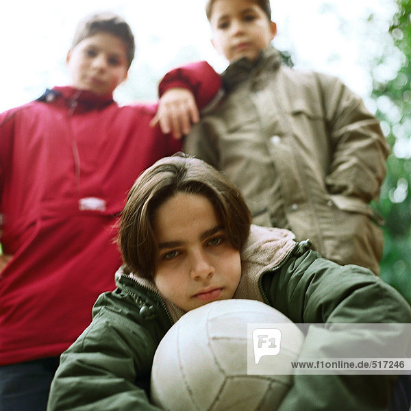 Drei Jungen draußen mit Blick auf die Kamera  ein Halteball  Blick in den niedrigen Winkel