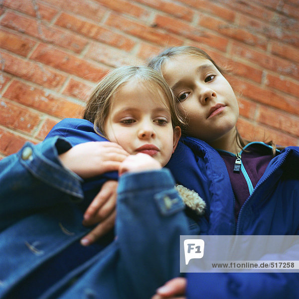 Zwei Mädchen  die sich umarmen  Backsteinmauer im Hintergrund  niedriger Blickwinkel