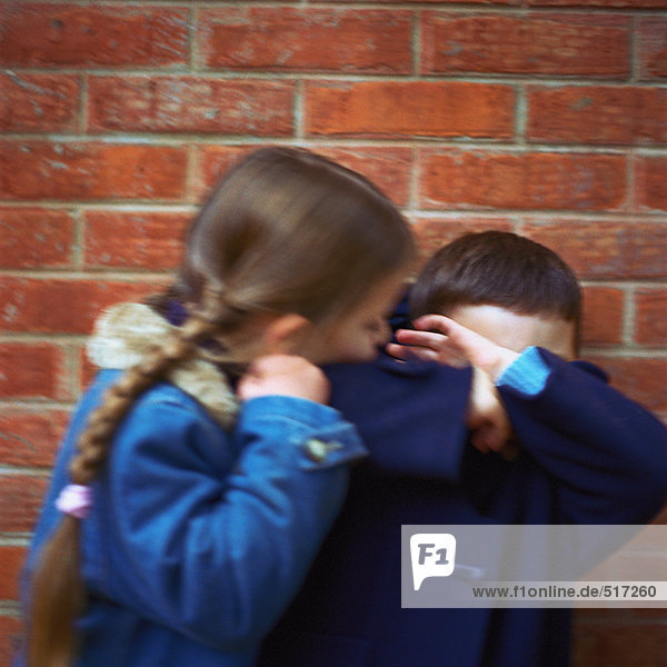 Mädchen  das versucht  den Jungen zu küssen  Junge  der das Gesicht mit Armen bedeckt  verschwommen