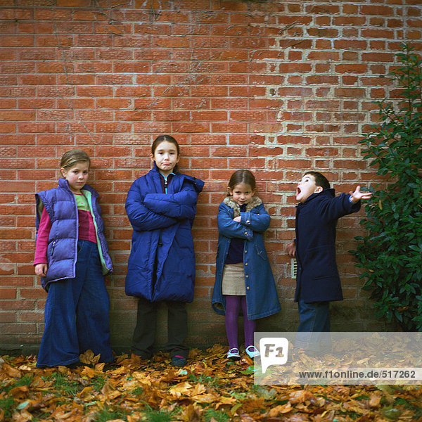 Vier Kinder in Mänteln vor der Ziegelwand  volle Länge