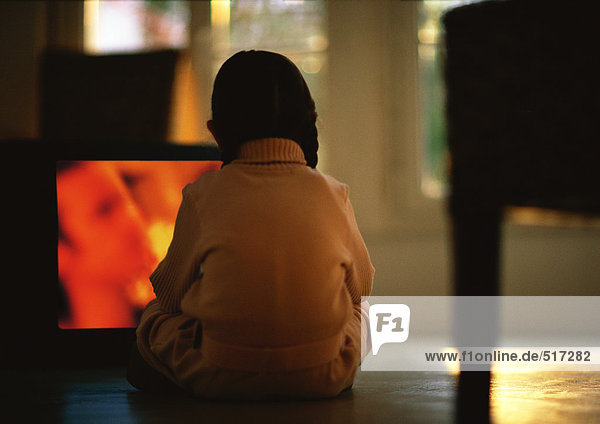Junges Mädchen sitzt auf dem Boden und schaut fernsehen  Rückansicht