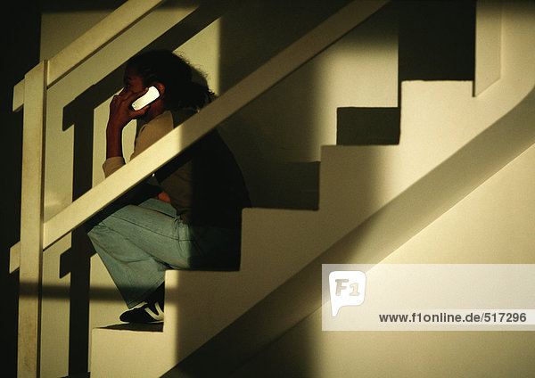 Junges Mädchen sitzt auf einer Treppe und telefoniert.