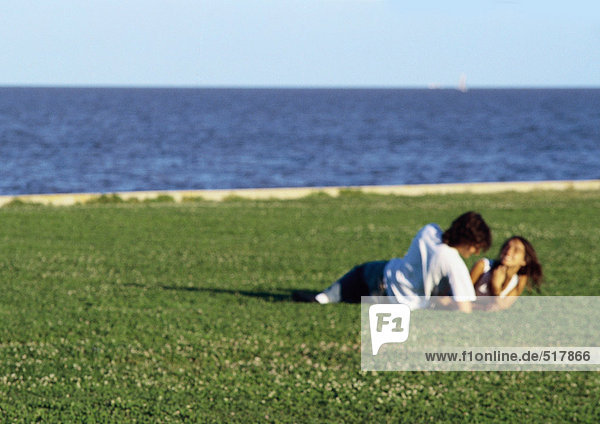 Junges Paar  zusammen auf Gras am Wasser liegend  verschwommen