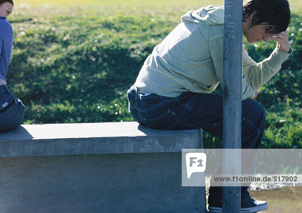 Teenager-Junge auf der Bank sitzend  mit dem Rücken zu seinem Freund  der seinen Kopf hält  Teilansicht
