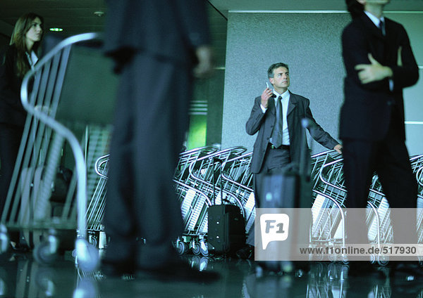 Eine Gruppe von Geschäftsleuten wartet  Mann an Mann mit Flughafen-Gepäckwagen per Handy.
