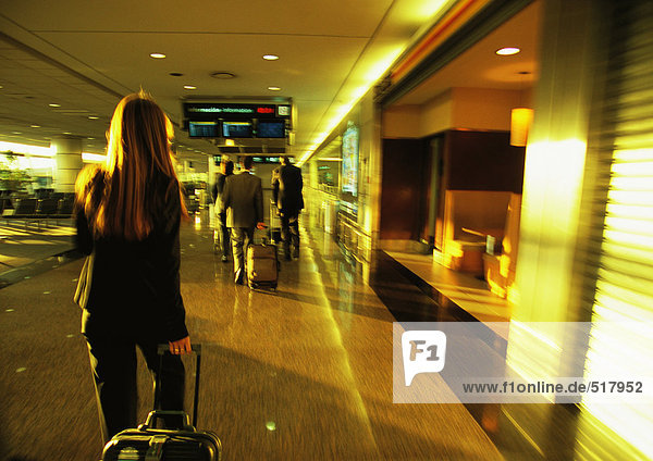 Businesswoman pulling suitcase through airport terminal.