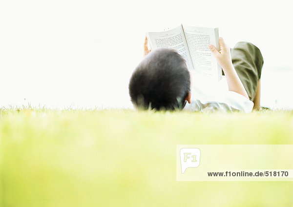 Kind auf dem Rücken auf Gras liegend  lesend  Rückansicht