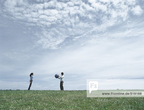 Junger Mann und Frau stehen auf Gras in der Ferne  Mann hält Ball