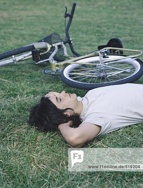 Junger Mann auf dem Rücken auf Gras neben dem Fahrrad liegend