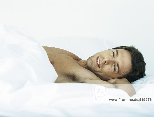 Man lying shirtless on bed looking at camera