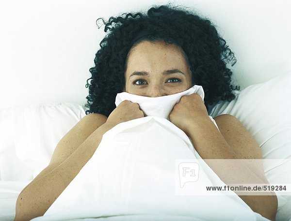 Frau im Bett versteckt Teil des Gesichts mit Decken