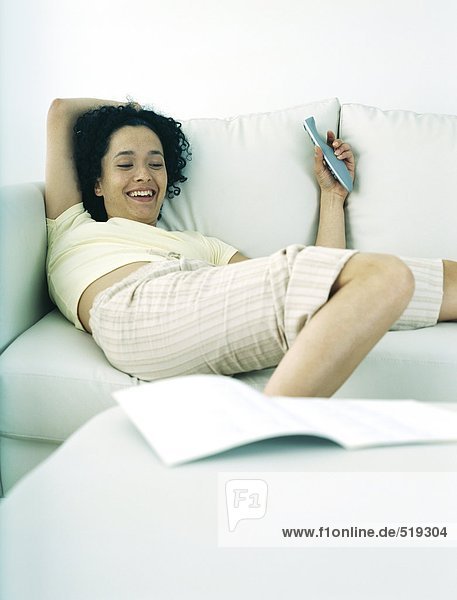 Woman lying on sofa holding remote control  smiling