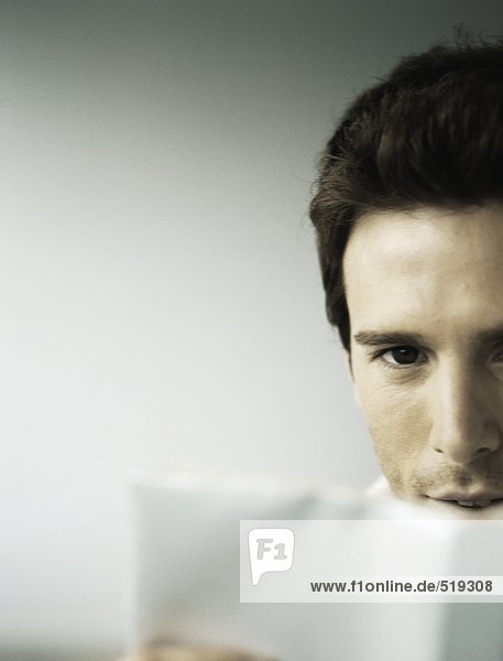 Man looking at camera from behind open book  partial view