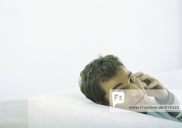 Mann sitzt auf dem Sofa  schaut zurück über die Schulter  hält Handy an Ohr