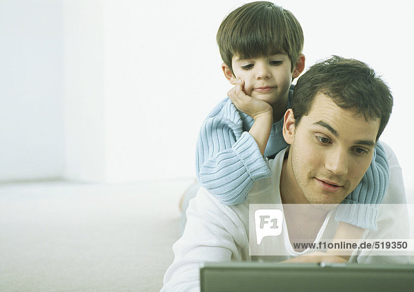 Kleiner Junge auf dem Rücken des Mannes  beide mit Blick auf den Laptop.