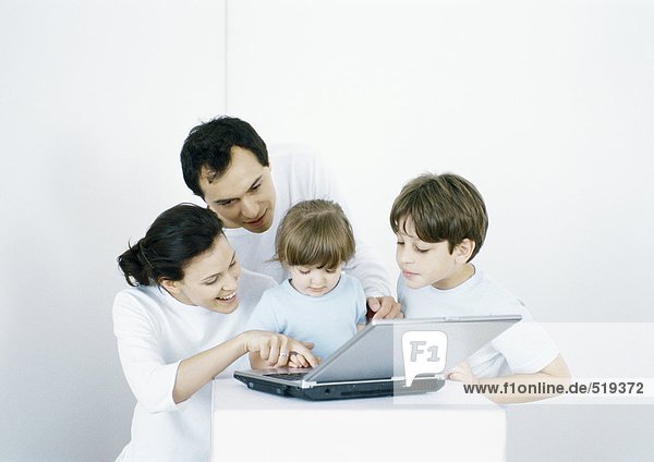 Junge und kleines Mädchen mit Eltern  die gemeinsam einen Laptop benutzen.