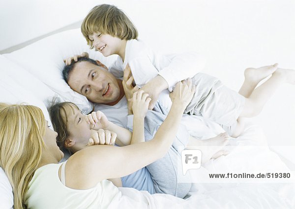 Eltern mit Tochter und Sohn im Bett,  lächelnd