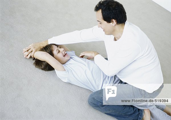 Man tickling boy on floor