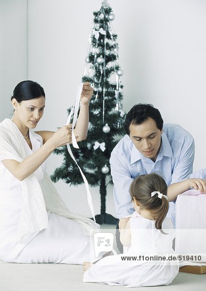 Little girl sitting on floor with parents near Christmas tree