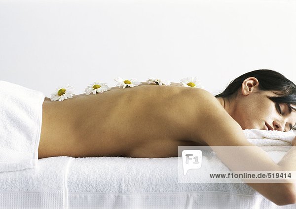 Frau auf dem Bauch liegend  Augen geschlossen  mit Gänseblümchen auf nacktem Rücken ausgerichtet  Seitenansicht