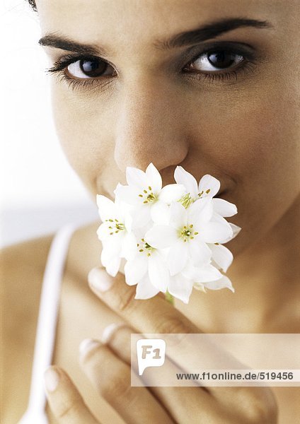 Frau hält weiße Blumen an die Nase  schaut in die Kamera  Nahaufnahme