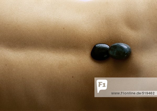 Frauenrücken mit schwarzen Steinen an der Basis der Wirbelsäule  Nahaufnahme