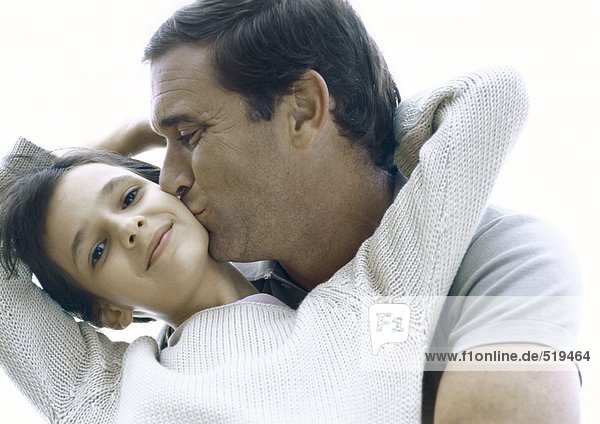 Girl reaching arms back around father's neck  father kissing girl's cheek
