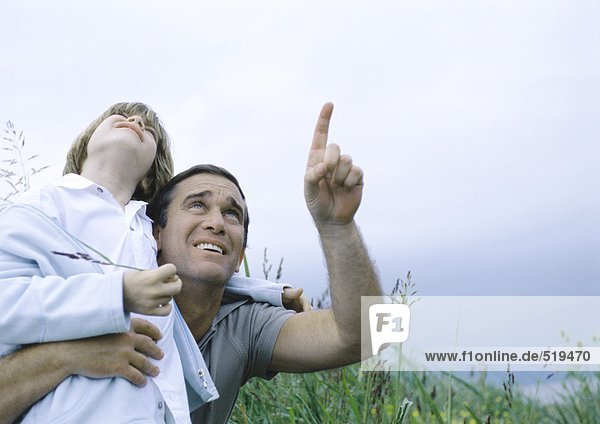 Mann hält den Sohn in den Armen und zeigt auf den bedeckten Himmel.