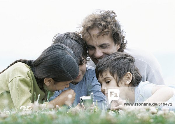 Mann mit Jungen und Mädchen auf Gras liegend mit Blick auf Handy  ebenerdig
