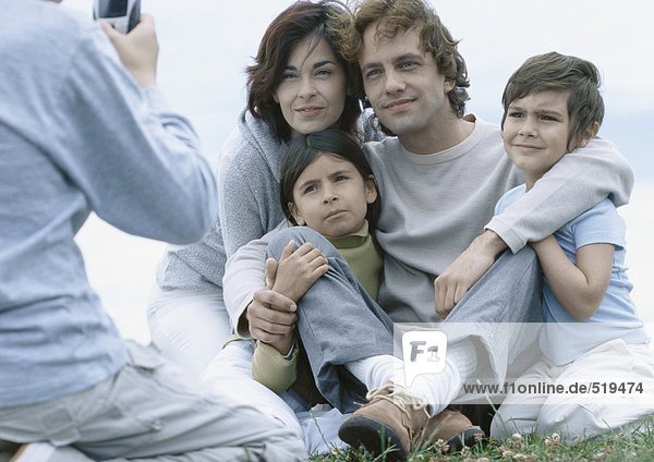 Eltern mit Junge und Mädchen  die auf Gras sitzen und für ein Foto posieren  Junge beim Fotografieren