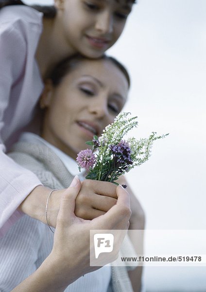 Mädchen umarmt Mutter von hinten  Mutterhand über Mädchen  mit Blumenstrauß