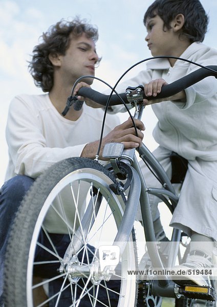 Junge auf dem Fahrrad mit Blick auf Vater  der sich am Fahrrad festhält.