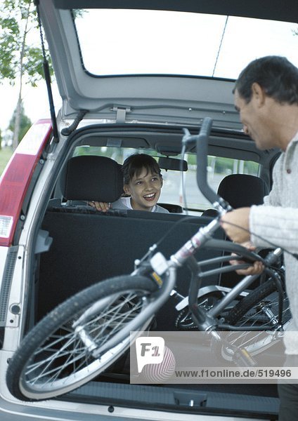 Mann stellt Fahrrad in den Kofferraum  Mädchen im Auto dreht sich um und lächelt den Mann an.
