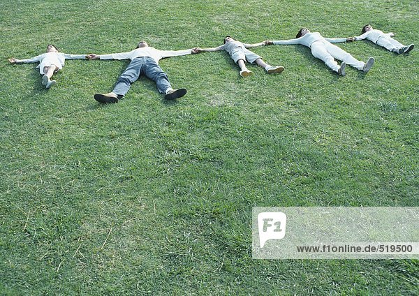 Eltern mit Jungen und Mädchen auf dem Rücken auf Gras liegend  mit ausgestreckten Armen  Händchen haltend