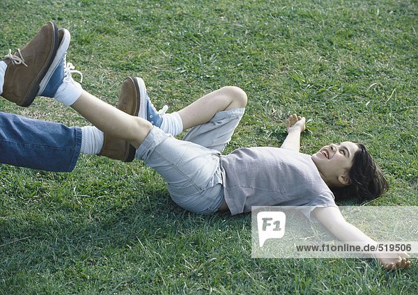 Junge auf dem Rücken auf Gras liegend  mit Füßen gegen die Füße des Menschen drückend