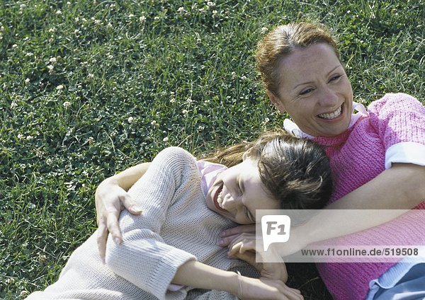 Frau und Tochter lachend auf Gras liegend